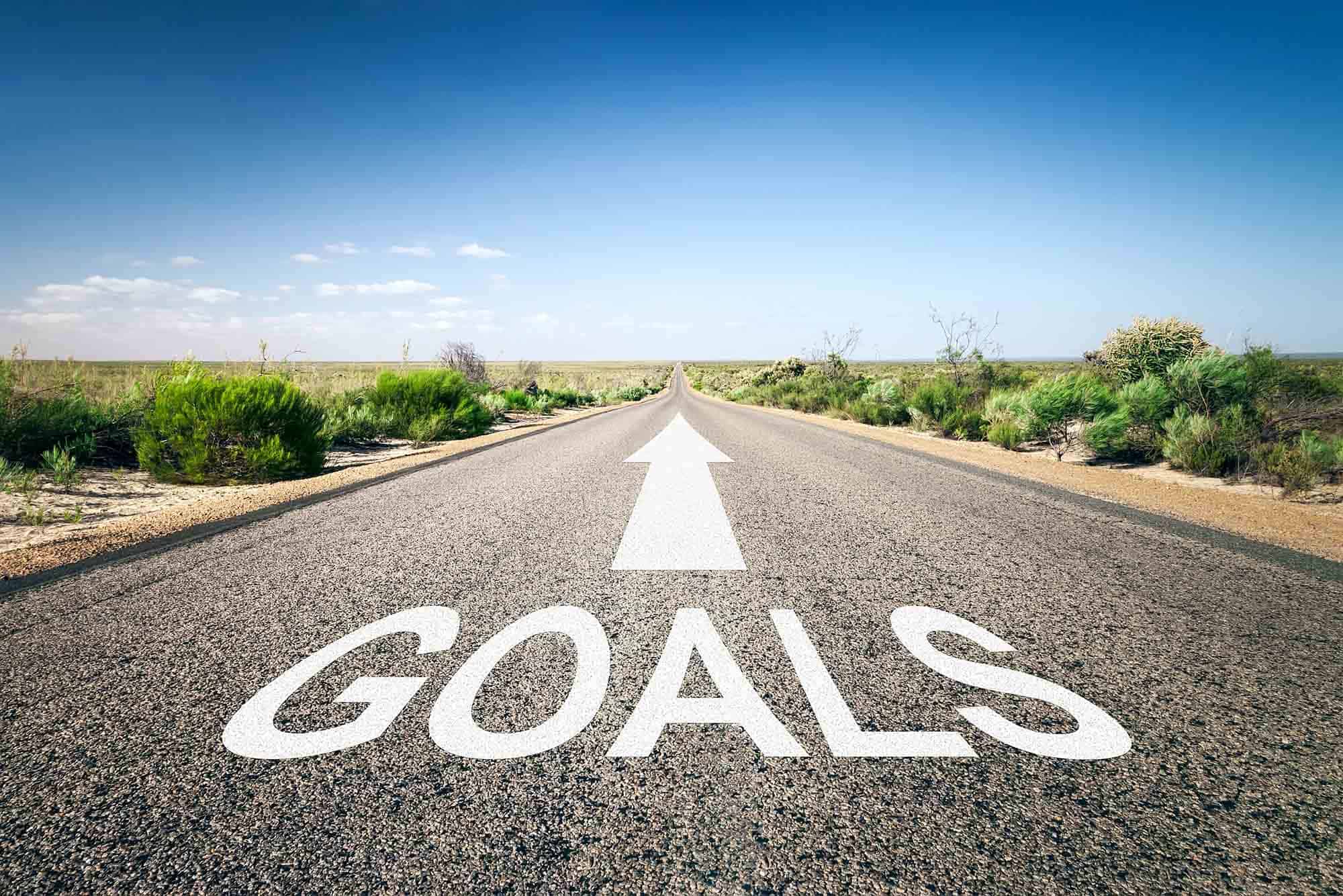A black, two land road in the desert with the word Goals painted on it.